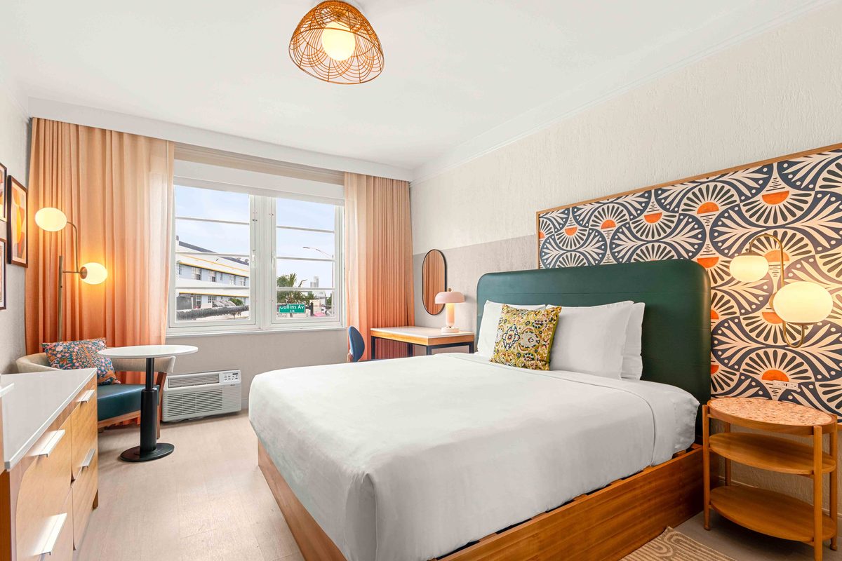 King Suite: a king bed with white linen against a teal headboard and a navy-and-orange fan-pattern wall panel, peach curtains at the window and a woven pendant light overhead