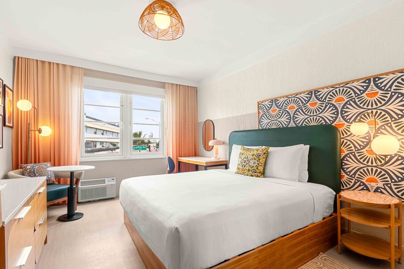 King Suite: a king bed against a teal headboard and a patterned Art Deco wall panel, with peach curtains at the window