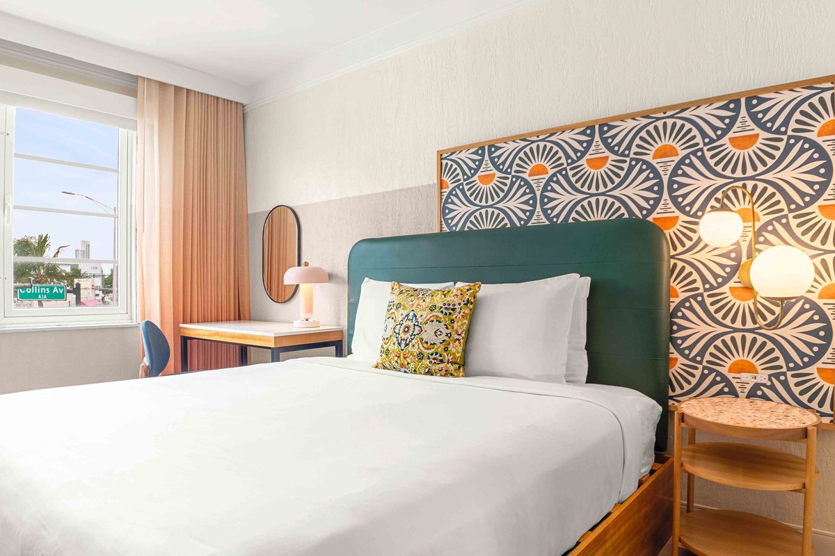King Suite seen from the foot of the bed, with the fan-pattern headboard panel, a wooden bedside table and a globe reading lamp