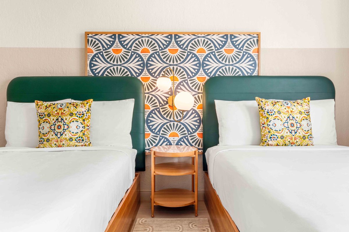 Standard Double Suite: the two beds side by side under the fan-pattern panel, with teal headboards, yellow patterned cushions and a small wooden table between them