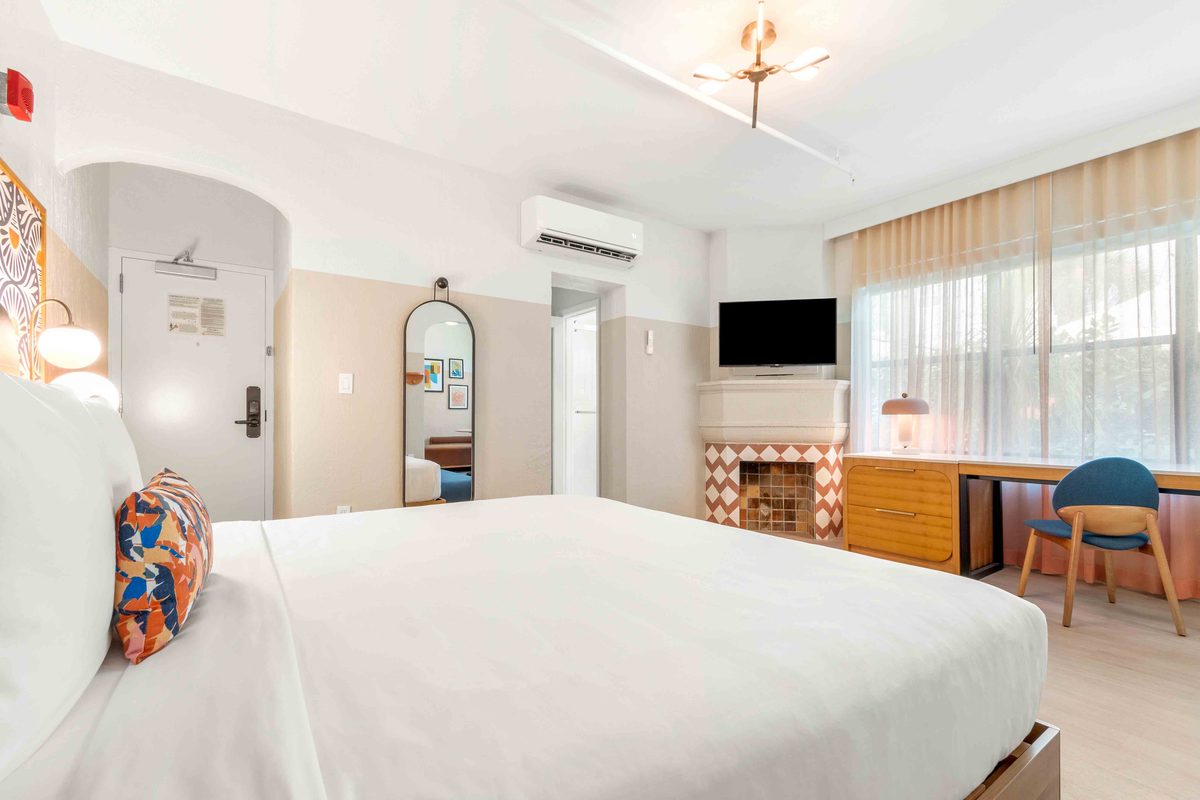 Superior Villa: a king bed in the foreground, an arched doorway to the bathroom, a tiled decorative fireplace with a television above it, and a desk by the window