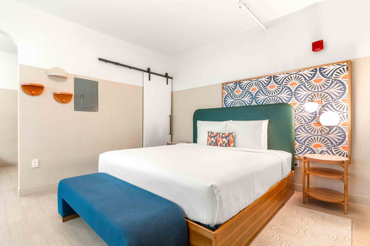 Superior Villa: a bed with a blue throw against the fan-pattern headboard panel, a sliding barn door on a black rail, and wall sconces either side