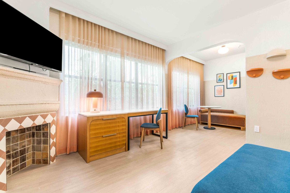 Superior Villa living end: the tiled fireplace with a pendant lamp, a desk with a blue chair, framed prints on the wall and the bed at the right