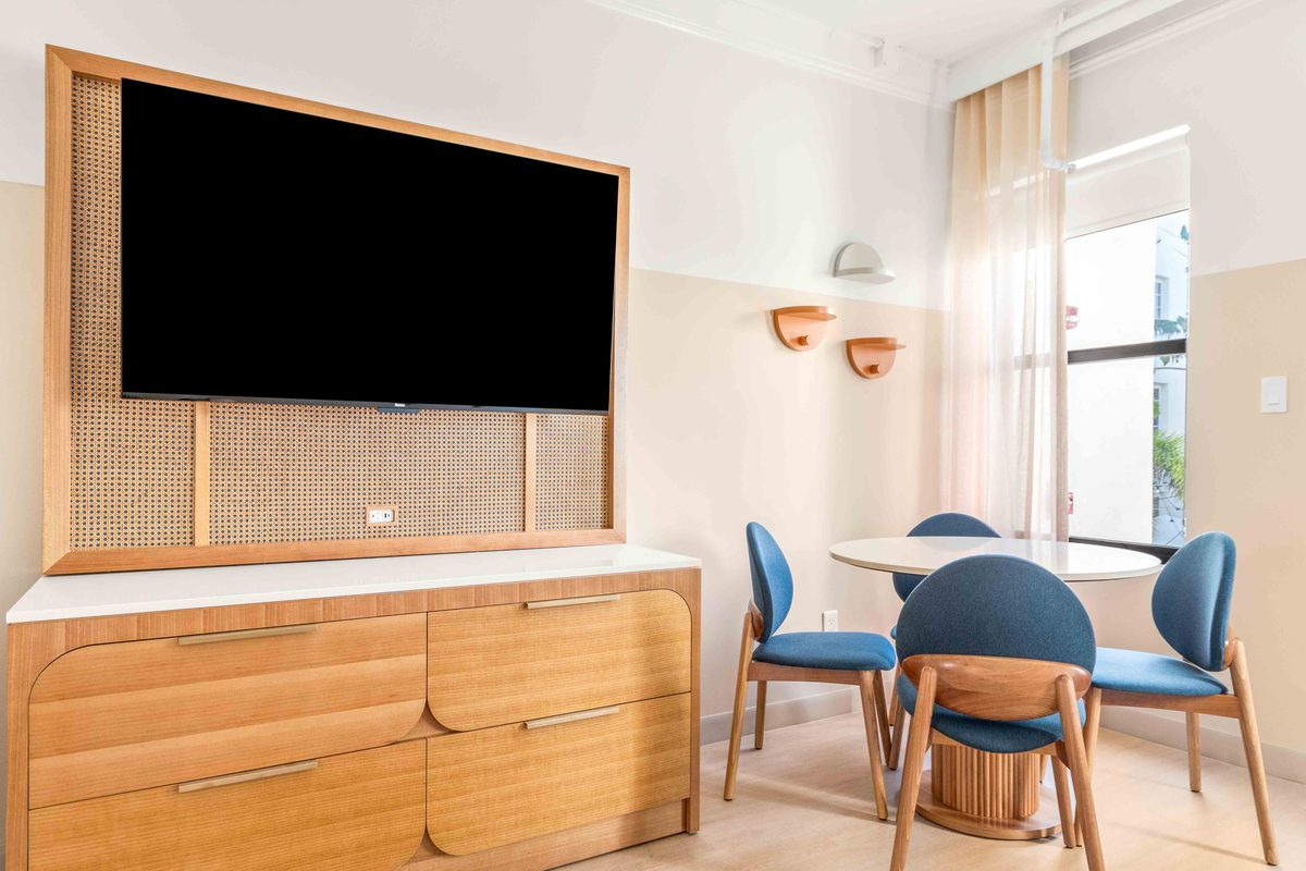 Two-bedroom Villa living area seen from the sofa, with the wall-mounted television, a curved wooden dresser, the round table with blue chairs and wall sconces